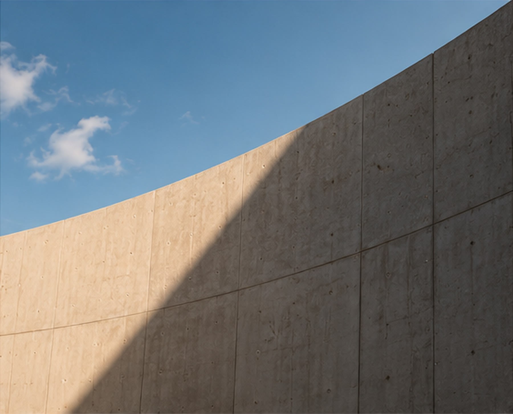 Curved concrete wall in raking light, with a dark shadow cutting diagonally across its surface.